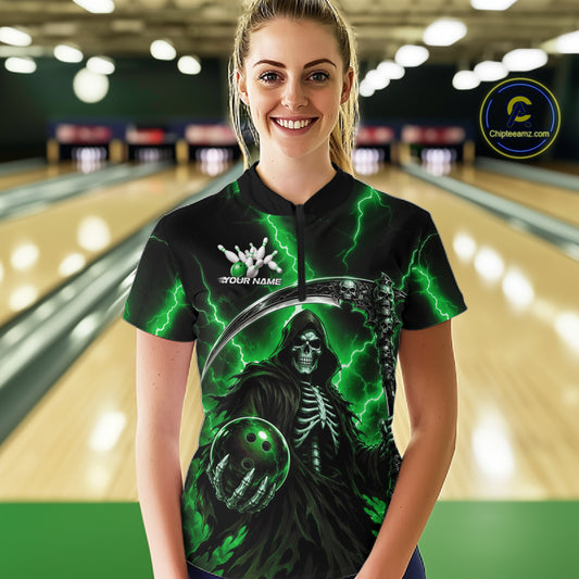 A woman stands in a bowling alley wearing a black short-sleeve bowling shirt with a green Grim Reaper graphic, lightning bolts, and a white 'YOUR NAME' text on the chest. The background shows blurred bowling lanes.
