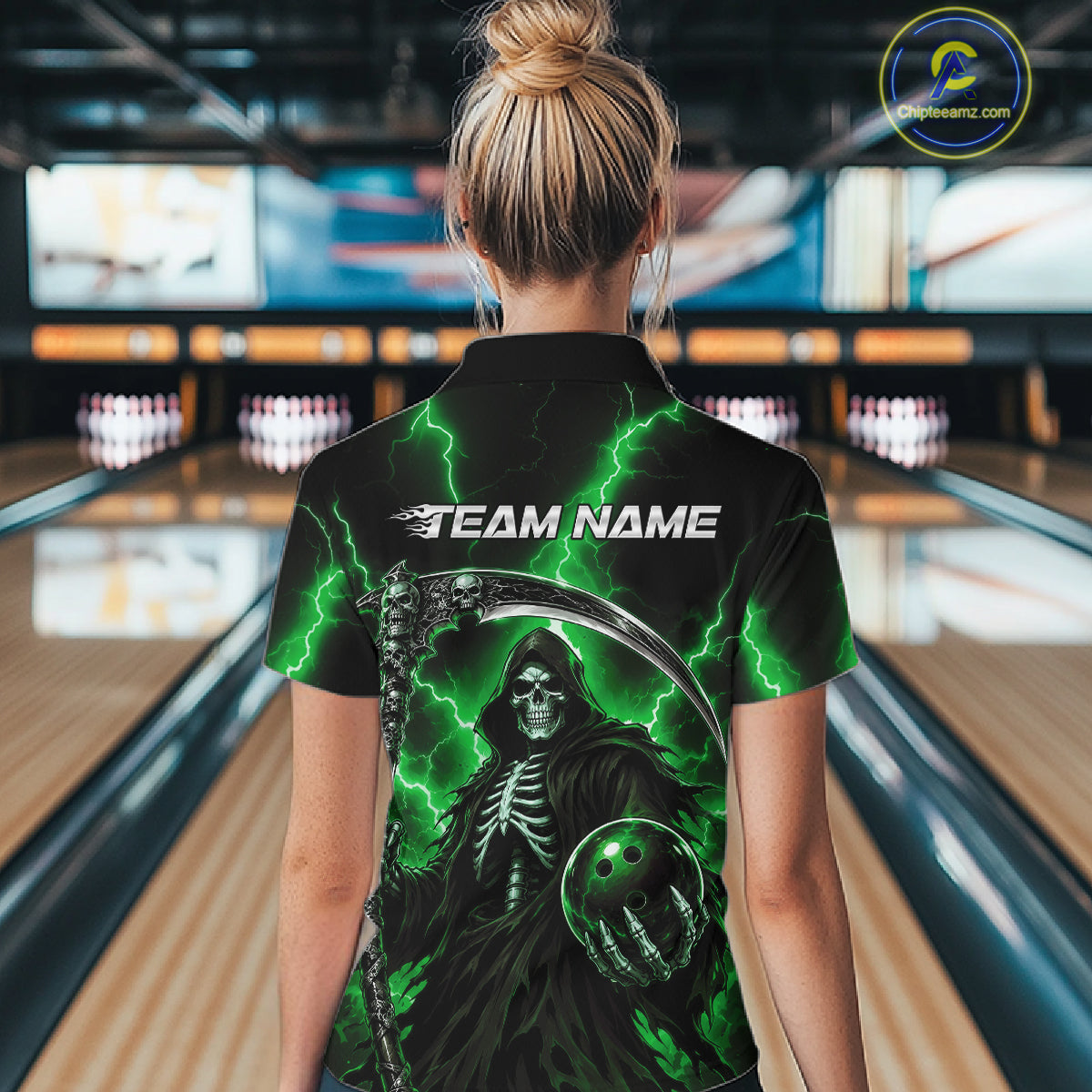 A woman viewed from behind wearing a black bowling shirt with a green and black grim reaper graphic, standing in a bowling alley.