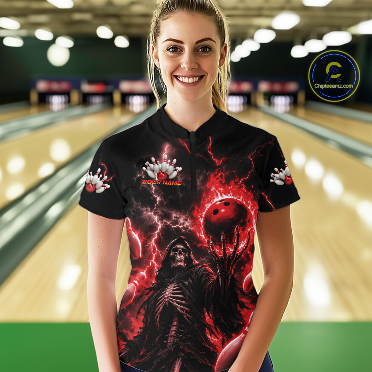 A woman stands in a bowling alley wearing a black short-sleeve polo shirt with a dramatic red and black graphic print featuring lightning, a skeletal figure, and a red bowling ball. 