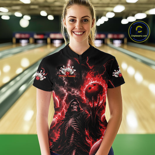 A woman stands in a bowling alley wearing a black short-sleeve polo shirt with a dramatic red and black graphic print featuring lightning, a skeletal figure, and a red bowling ball. 