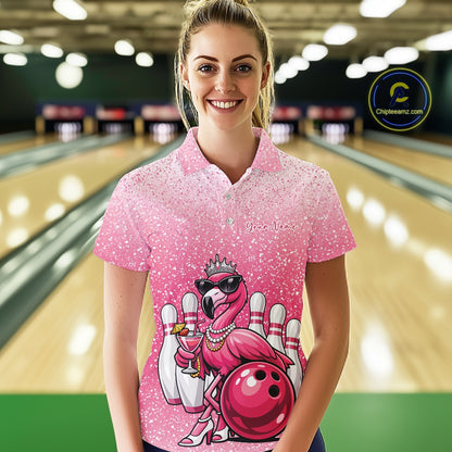 Female model at a bowling lane wearing a pink bowling polo shirt with a crowned flamingo holding a cocktail and resting against a bowling ball.