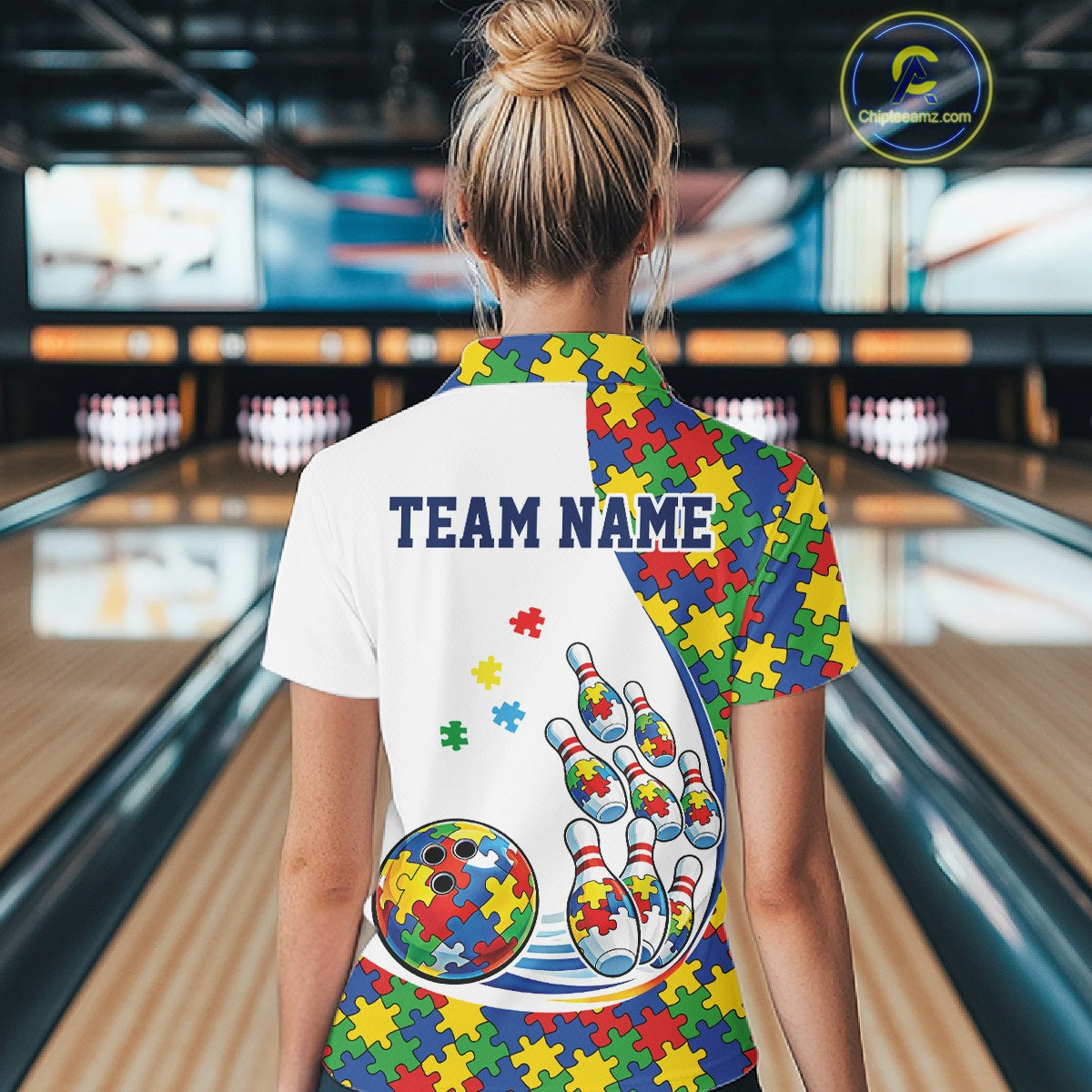 Female model at a bowling lane, back view of white polo shirt featuring autism puzzle bowling strike design with multicolor details