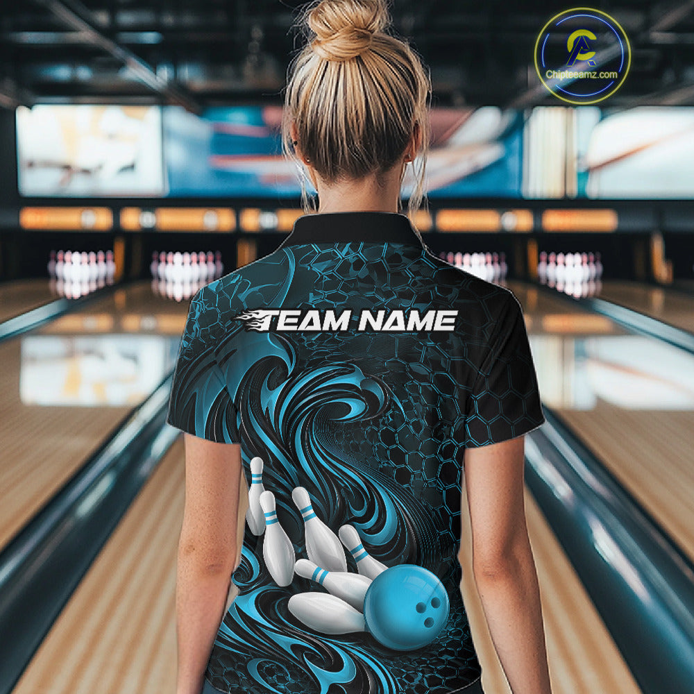 Female model standing in a bowling lane showing the back of a black and blue bowling polo shirt with a tribal flame bowling ball and pins graphic.