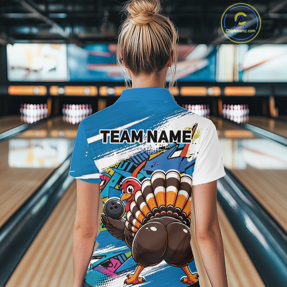 Back view of a female model wearing a blue custom bowling polo shirt with a funny graffiti turkey holding a bowling ball, paint splatter accents, and a personalized name in a bowling alley.