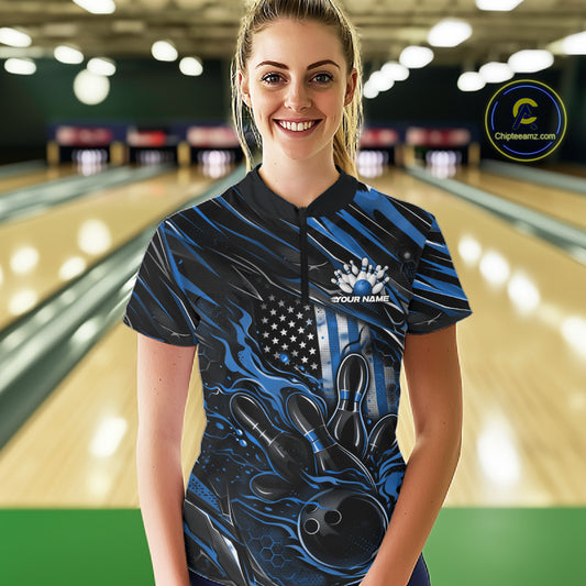 Female model in a bowling alley wearing black and blue quarter zip shirt, front view featuring patriotic flaming bowling ball knocking down pins dynamic illustration