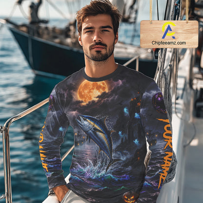 A man wearing a long-sleeve graphic shirt with a detailed print of a tuna fish leaping from the water under a full moon, set on a boat deck. A wooden sign with the text 'Chipleeamz.