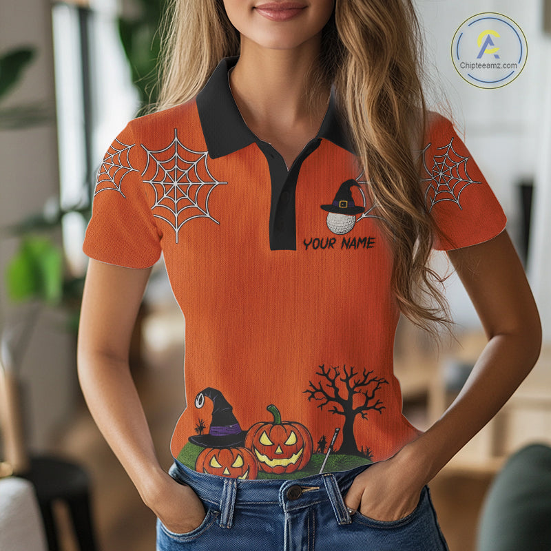 A woman wearing a bright orange short-sleeve polo shirt with a black collar and Halloween-themed graphic print, including spiderwebs, pumpkins, a witch, and a bare tree. The shirt has a customizable name printed on the chest.