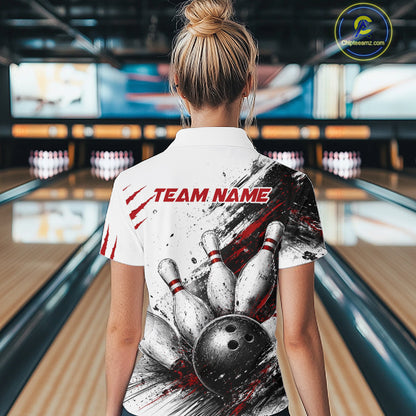 A woman viewed from behind wearing a white short-sleeve bowling-themed polo shirt with a large graphic of bowling pins, a bowling ball, and red 'TEAM NAME' text, standing in a bowling alley.