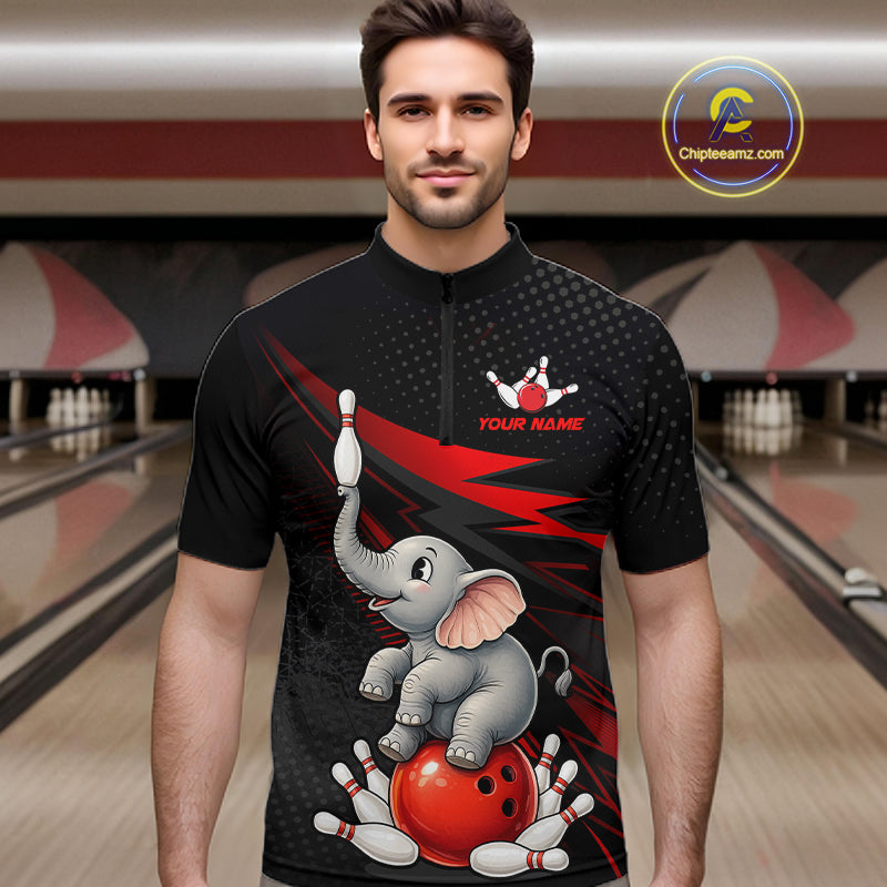 A man wearing a black short-sleeve quarter-zip bowling-themed t-shirt with a cartoon elephant, red bowling ball, and white pins printed on the front. The background shows a blurred bowling alley with lanes and pins.
