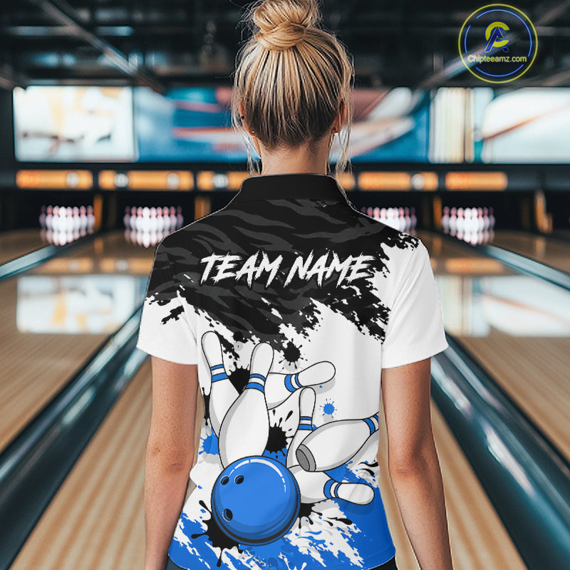 A woman viewed from behind wearing a custom bowling-themed polo shirt in a bowling alley. The back of the white and black polo features a graphic of bowling pins, a blue bowling ball, and the text 'TEAM NAME'