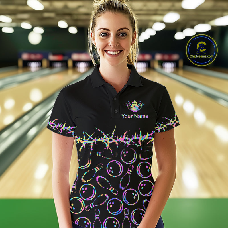 A woman standing in a bowling alley wearing a black short-sleeve polo shirt with a colorful bowling-themed print of bowling pins and balls, a white 'Your Name' placeholder on the chest, and a logo on the left chest