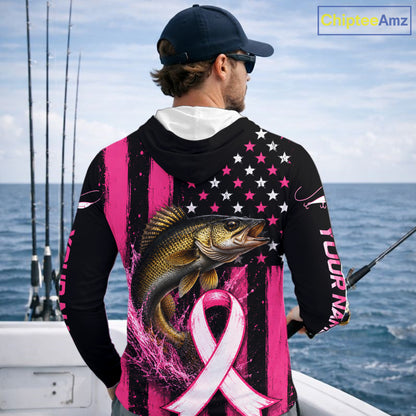A man wearing a black and pink long-sleeve hoodie with a walleye fish graphic and pink ribbon design on the back, standing on a boat with fishing rods and the ocean in the background.