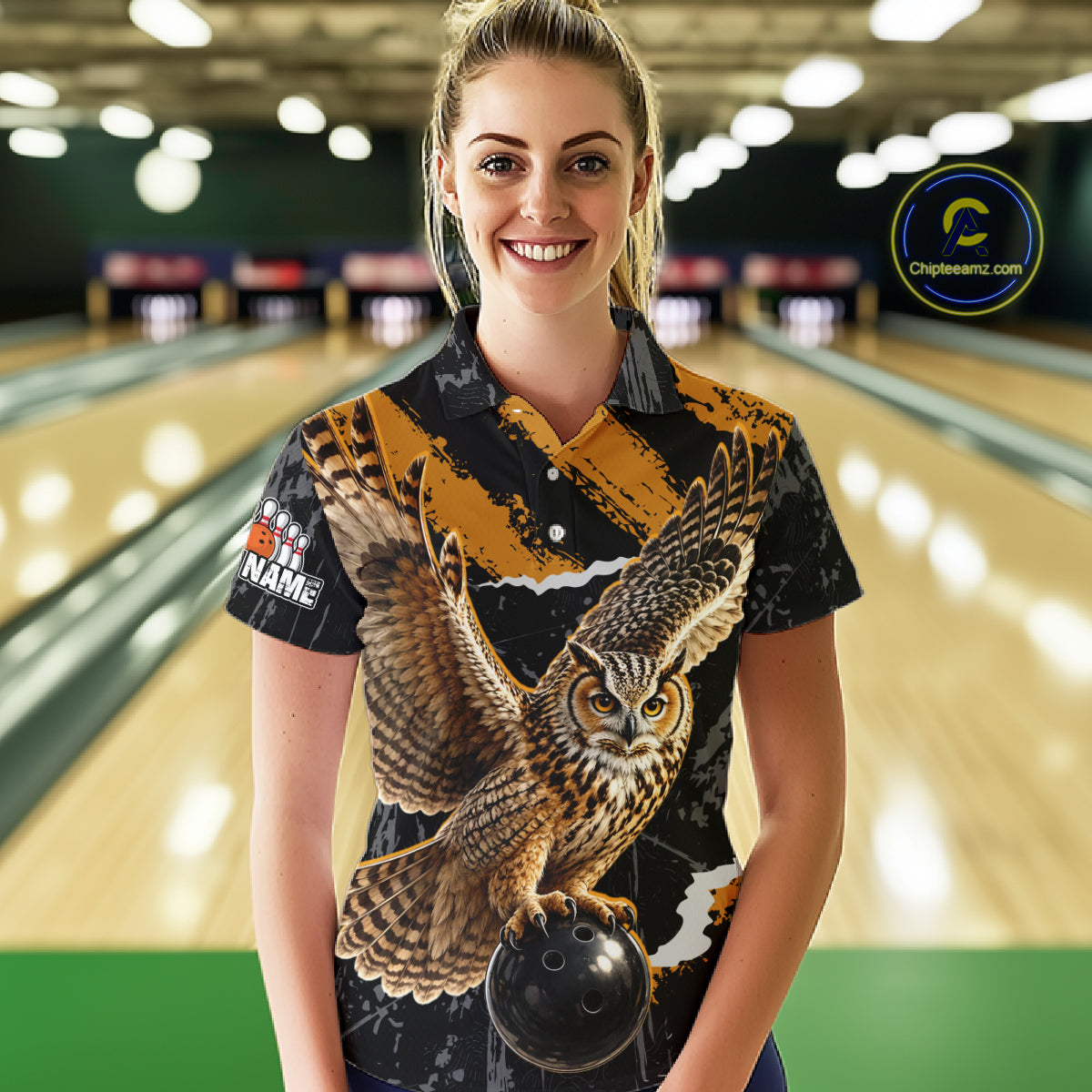 A woman standing in a bowling alley wearing a short-sleeve button-up shirt with a large owl graphic on the front, holding a bowling ball. The shirt has a black base with a bold owl print in brown, beige, and white, and a bowling pin graphic on the sleeve.