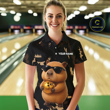 Load image into Gallery viewer, Woman wearing a black bowling shirt with a capybara design in a bowling alley.